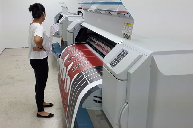Woman Observing Machine Printing Sublimation Prints on Large Sheet