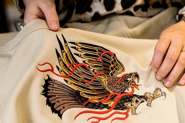 Hands Holding Jacket with Stitched Embroidery of a Colorful Eagle Design