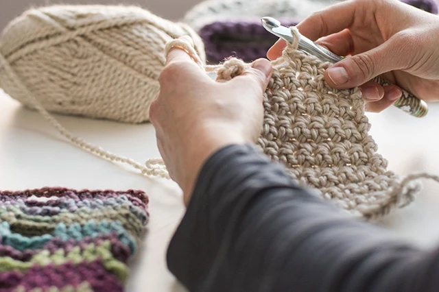 Hands Crocheting Beige Yarn with Finished Pieces Nearby